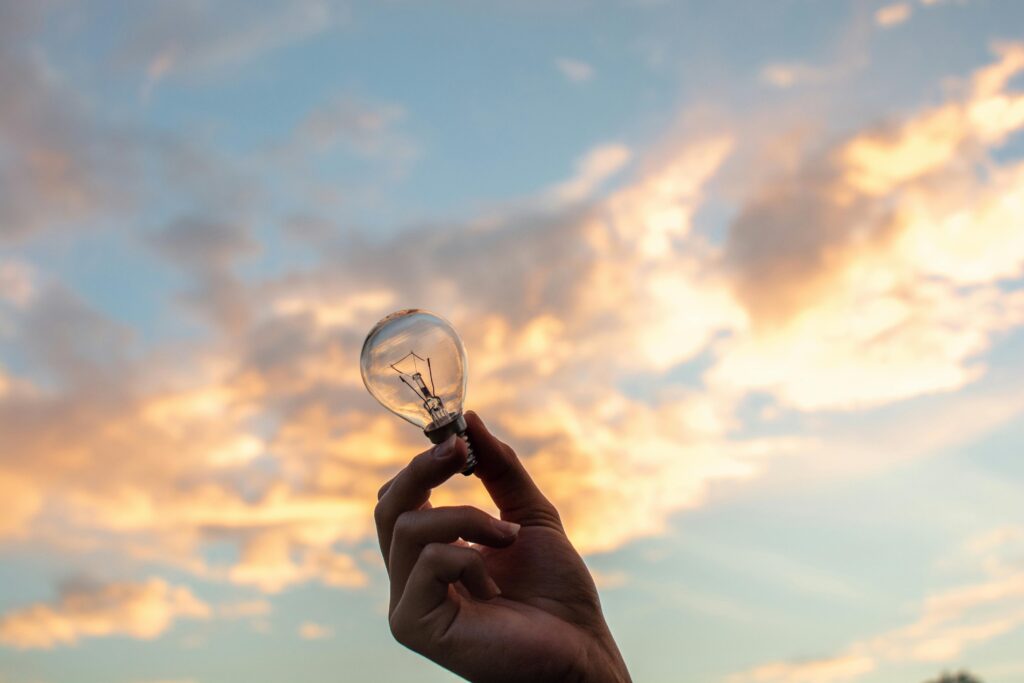 A hand holds a light bulb against a scenic sunset sky, symbolizing creativity and innovation.